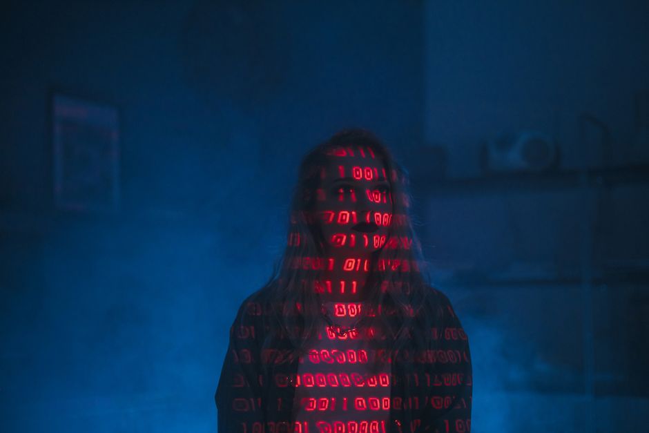 A close-up view of a laptop on a wooden table displaying lines of colorful coding text on its screen. Next to the laptop, there is a ceramic coffee mug with a beige background featuring black text tha