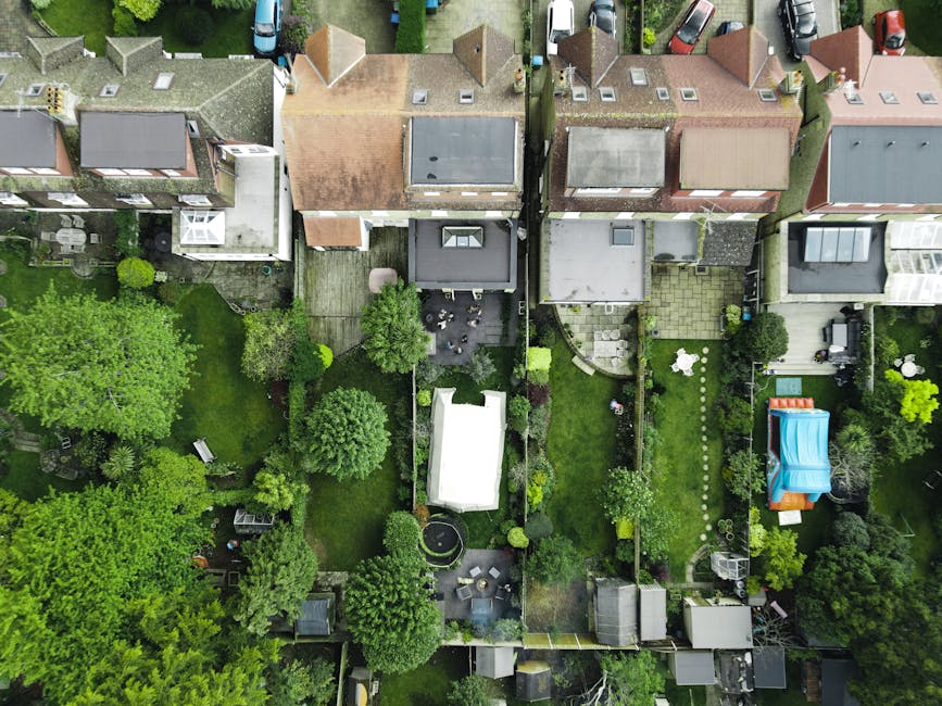 An aerial view of multiple residential back gardens in Southgate N14, showing a variety of landscaping features, including well-maintained lawns, garden beds with flowering plants, paved patios, and t